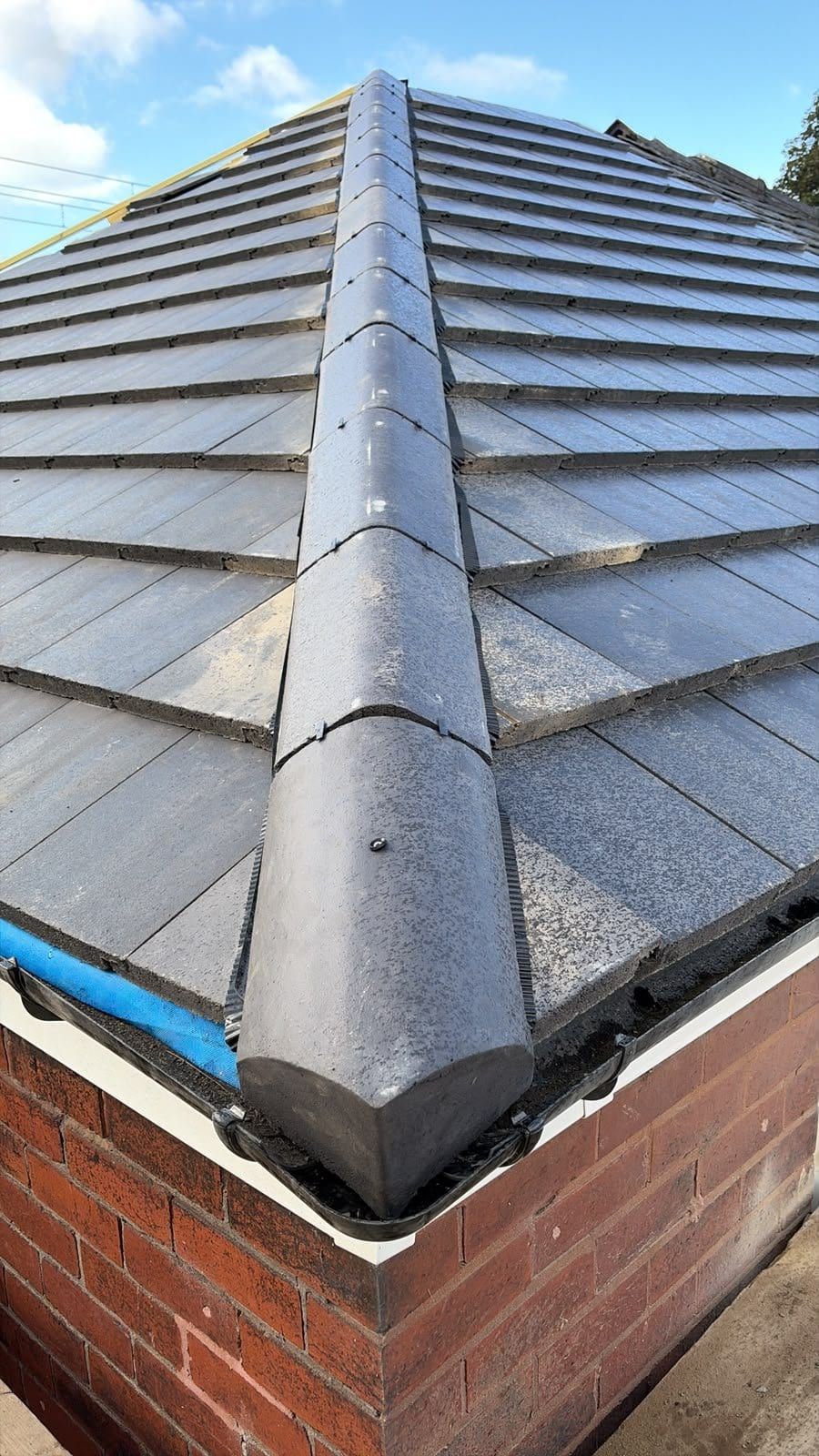 A close view of a dry fixed hip ridge running down a new grey tiled roof