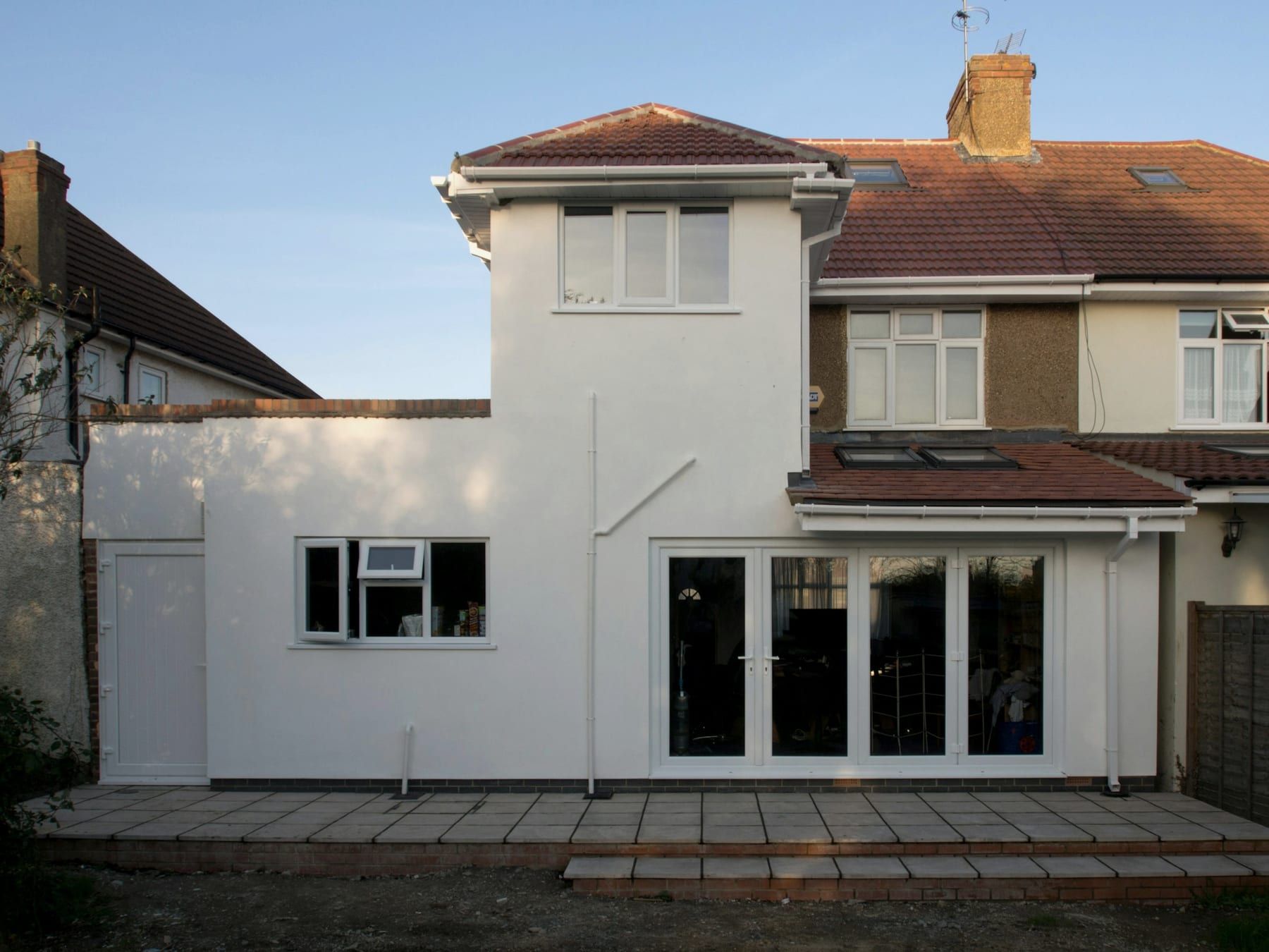 The back of a semi-detached house with a white rendered rear extension with a flat roof and patio doors