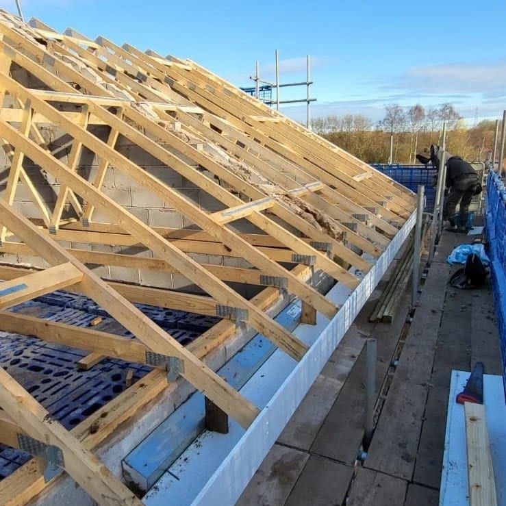 New timber roof trusses fixed along the top of a new building, with scaffold along the side