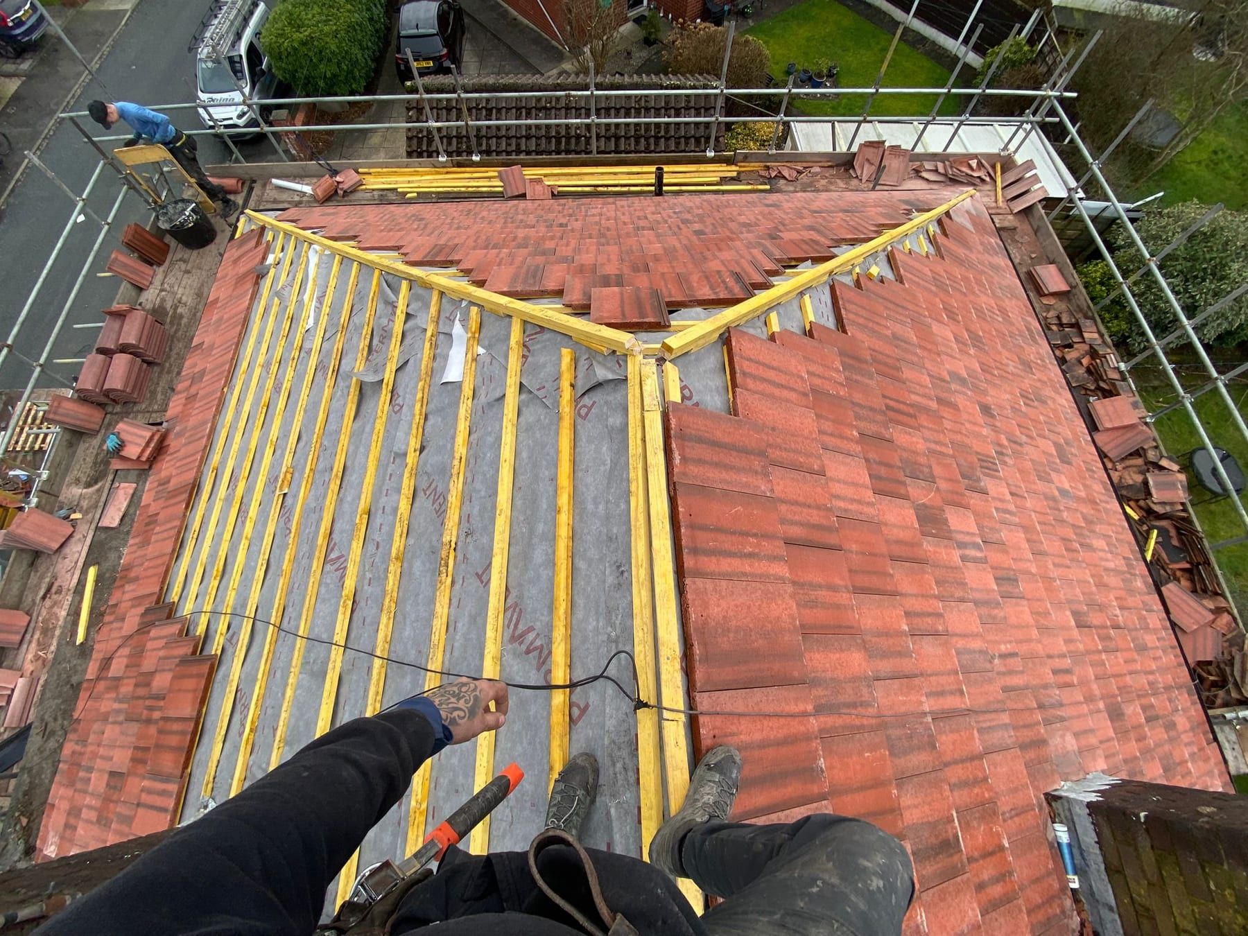A red tiled hip roof being re-battened, with new battens across one slope and the old tiles on the other
