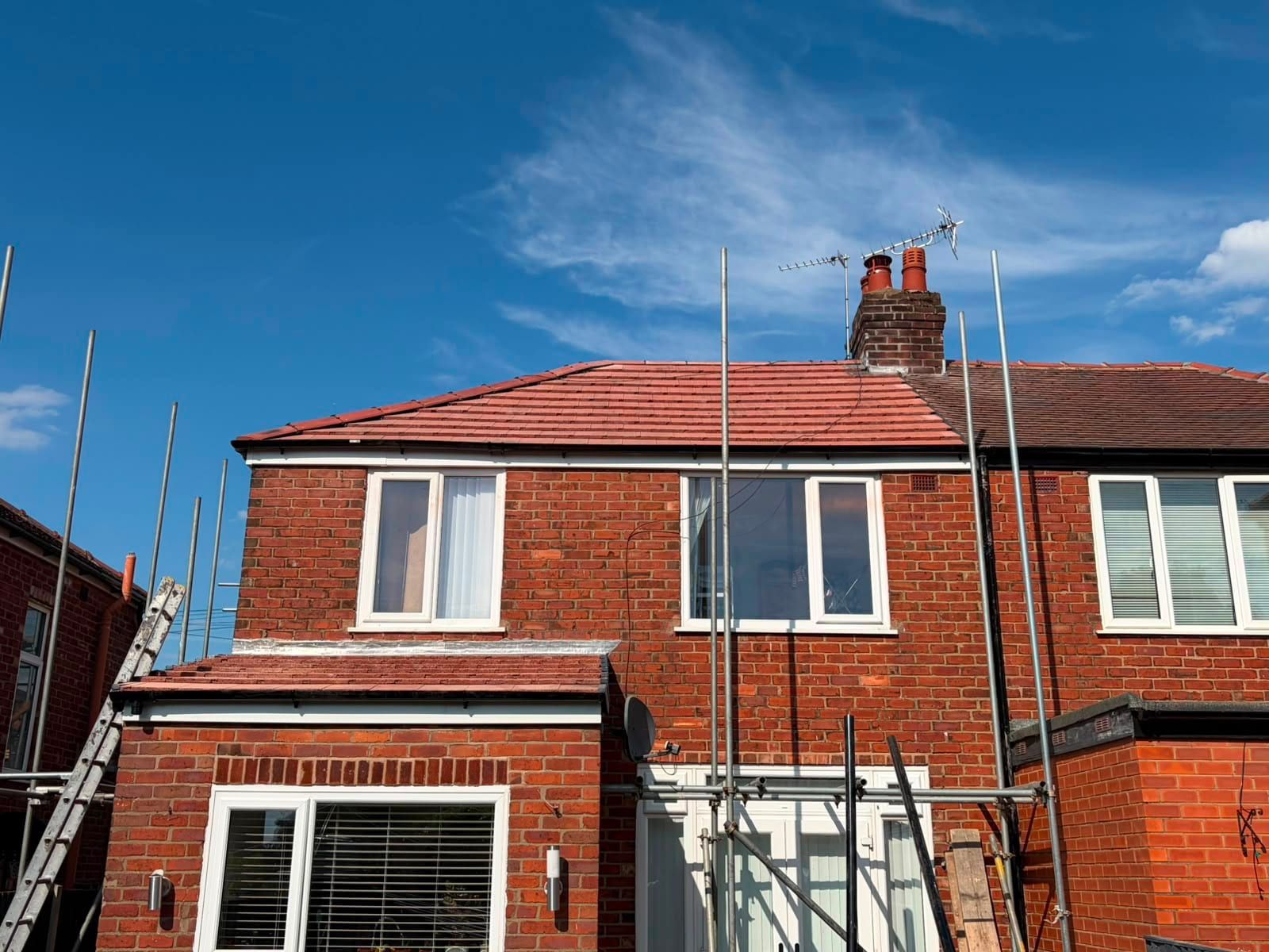 The back of a red brick semi-detached house with a new red tiled roof and scaffolding still in place