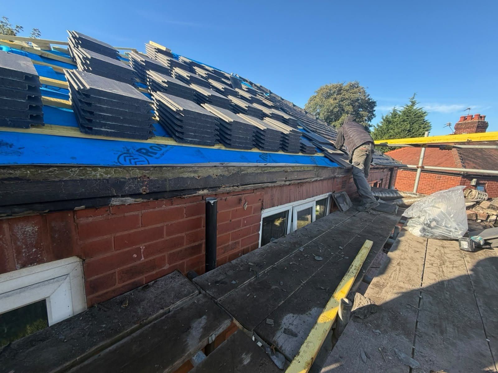Stacks of new grey roof tiles loaded out on fresh battens over blue membrane, ready to be laid
