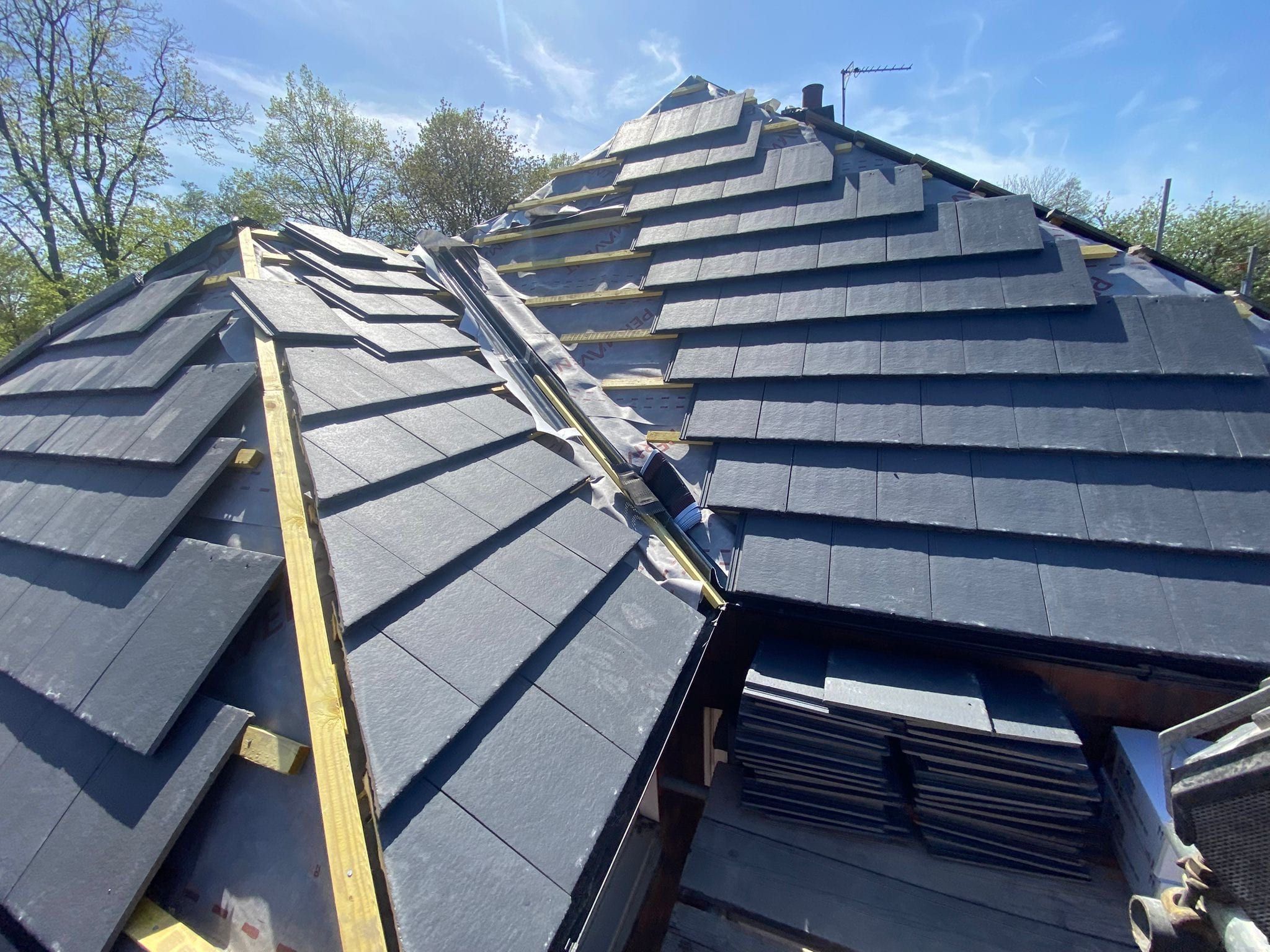 New dark grey tiles being laid up a hip roof over fresh timber battens, with the hip line still open